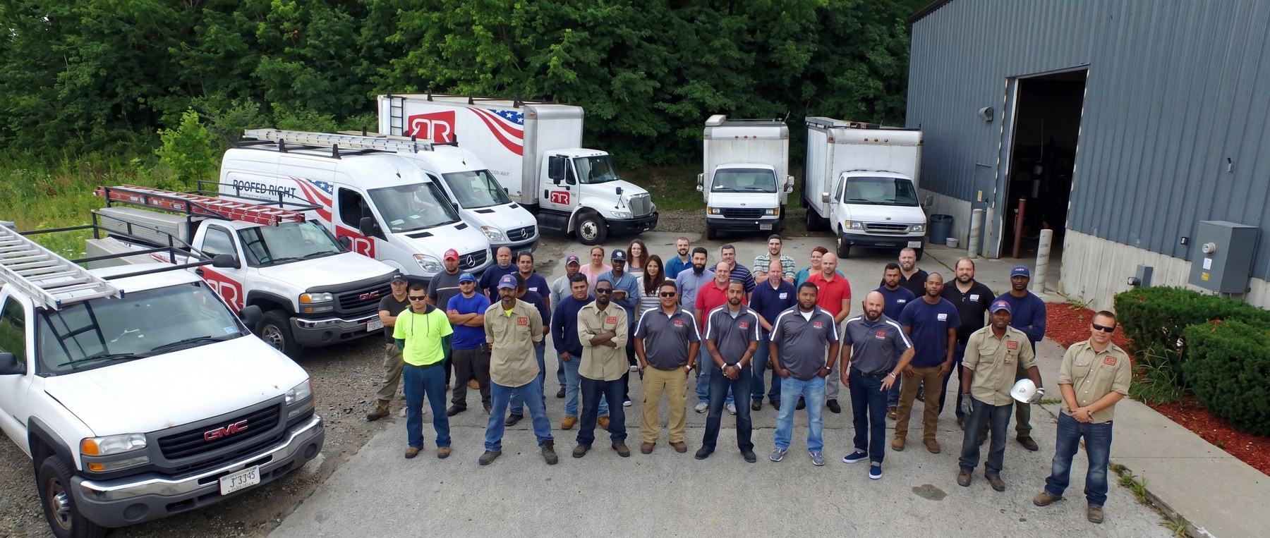 A roofing crew of about forty people lined up in front of company trucks
