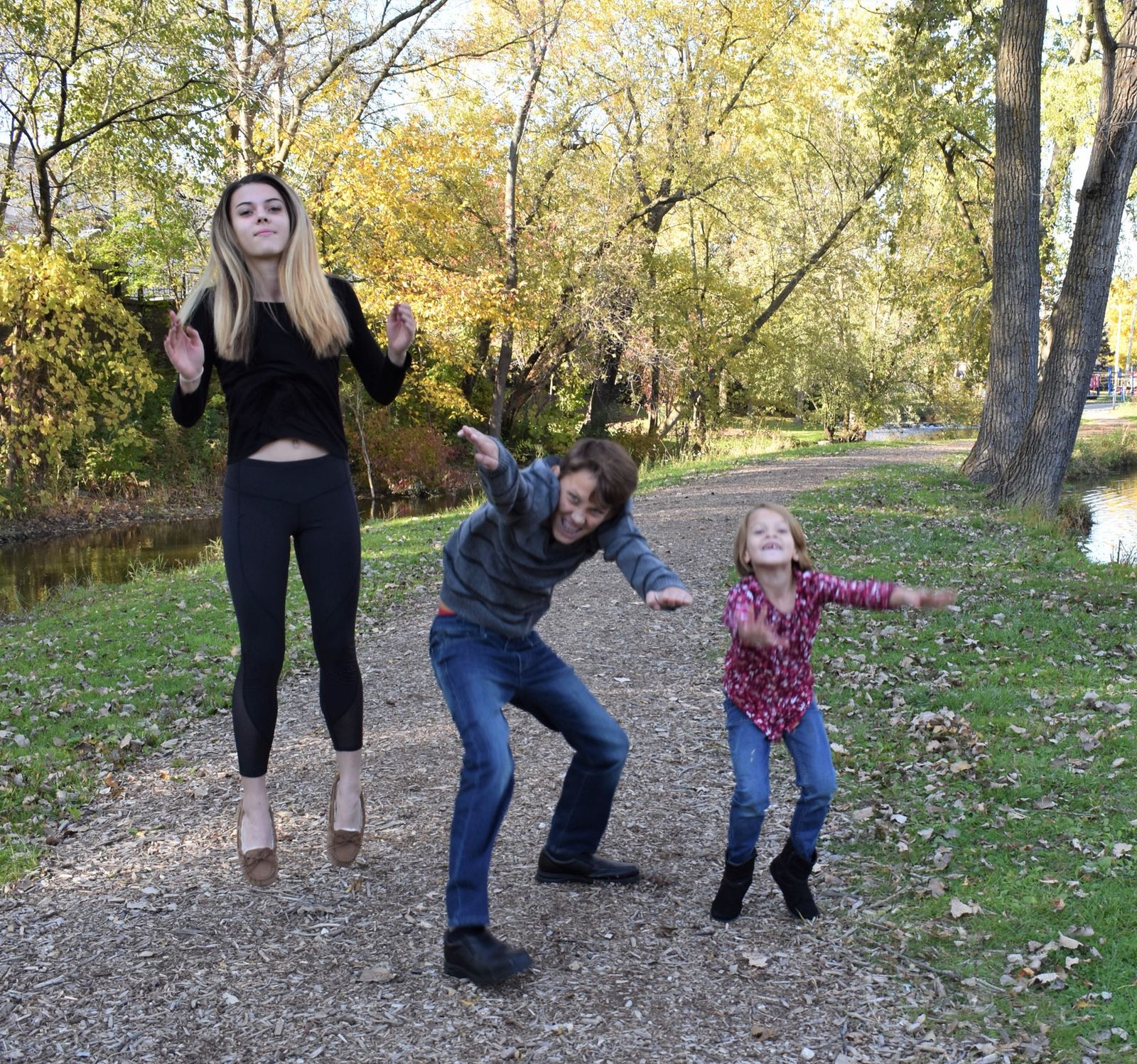 Khary's three kids jumping on a wooded path