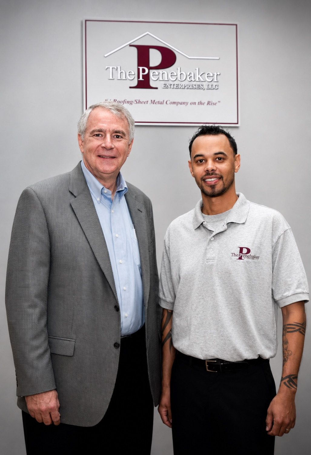 Khary in a Penebaker Enterprises polo standing beside an older man in a suit under the company sign